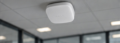 White rounded-square Ajax EN54 detector on an office ceiling, from the approved artwork